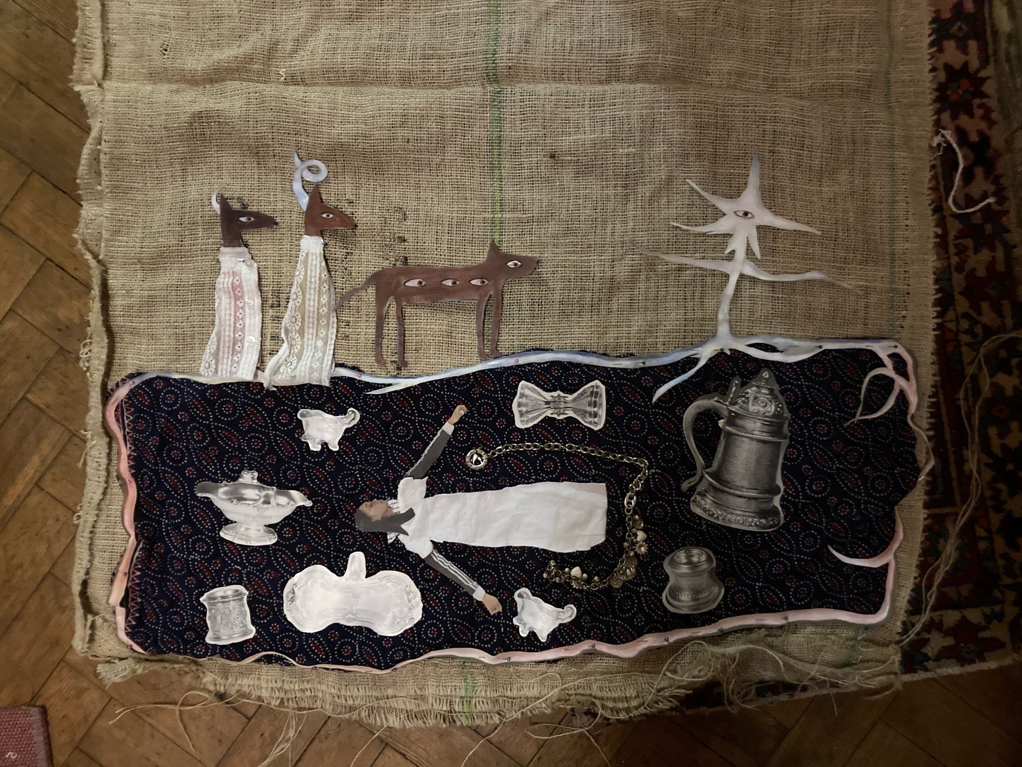 Assemblage of found objects and miniature figures arranged on patterned fabric and burlap