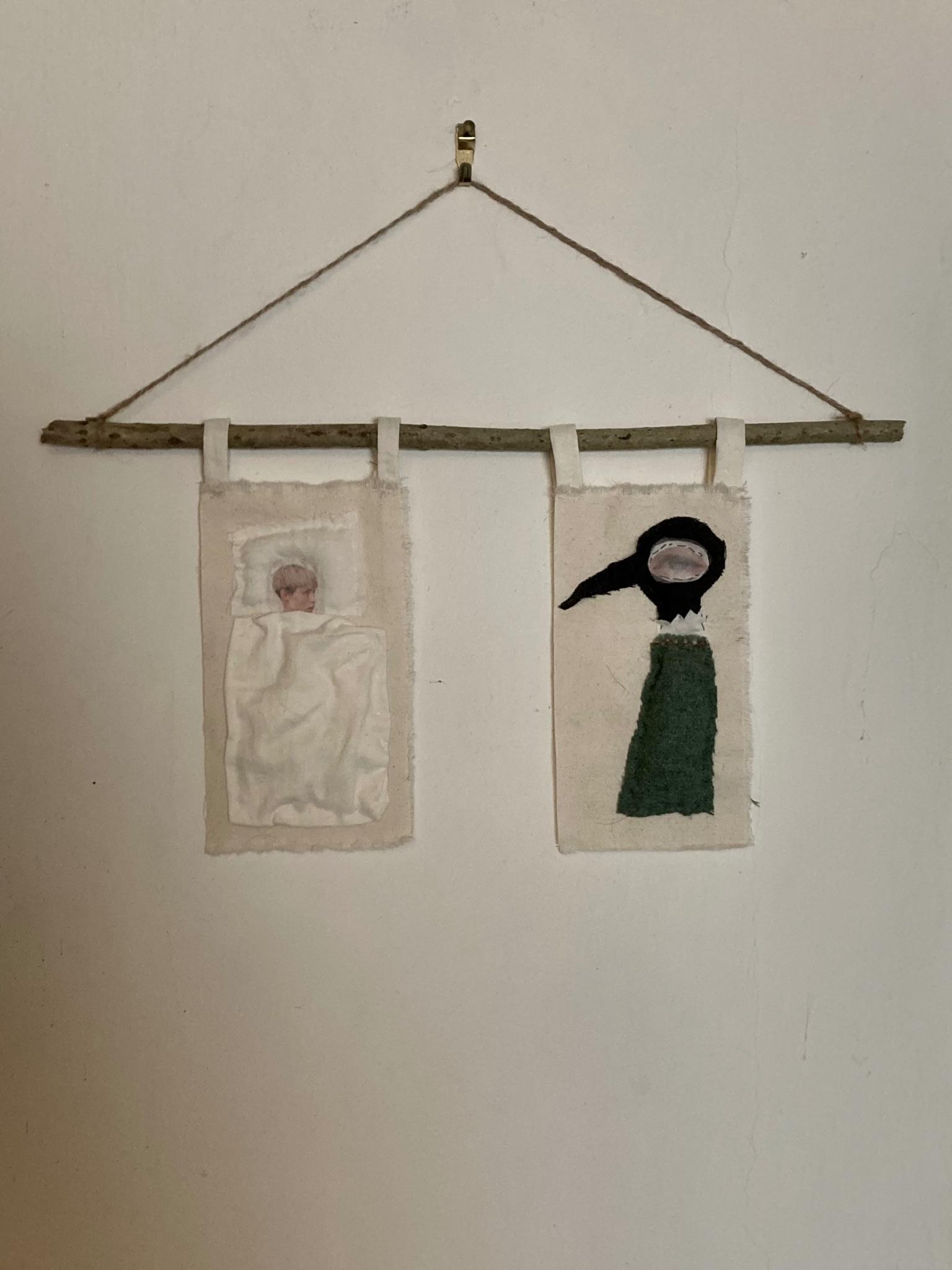 Textile flagpole piece hanging on a wall, two fabric panels with figures suspended from a branch